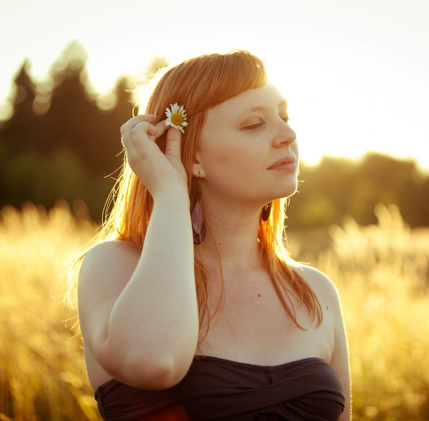 a girl putting a flower behind her ear in a meadow.