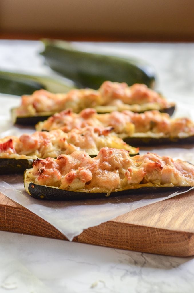 Close up image of four crab and artichoke stuffed zucchini on wax paper and wooden cutting board