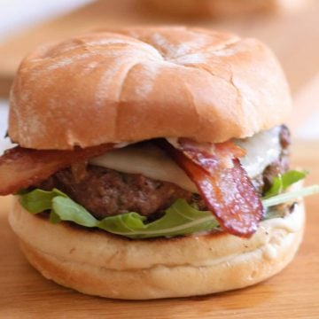 A caramelized onion burger with bacon sticking out of it.
