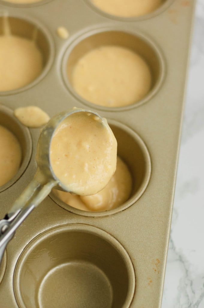 A cupcake scoop dropping batter into a muffin tin.