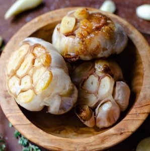 Close up of three heads of roasted garlic inside a wooden bowl.