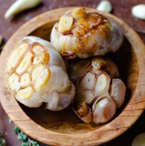 Close up of three heads of roasted garlic inside a wooden bowl.