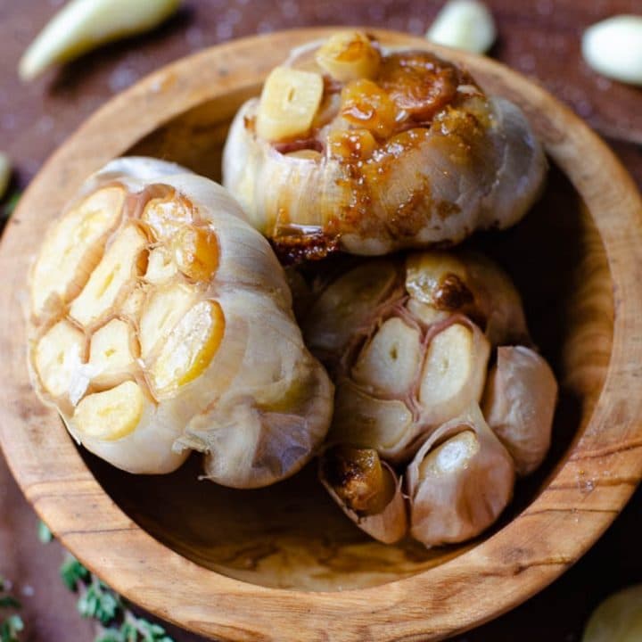 Close up of three heads of roasted garlic inside a wooden bowl.