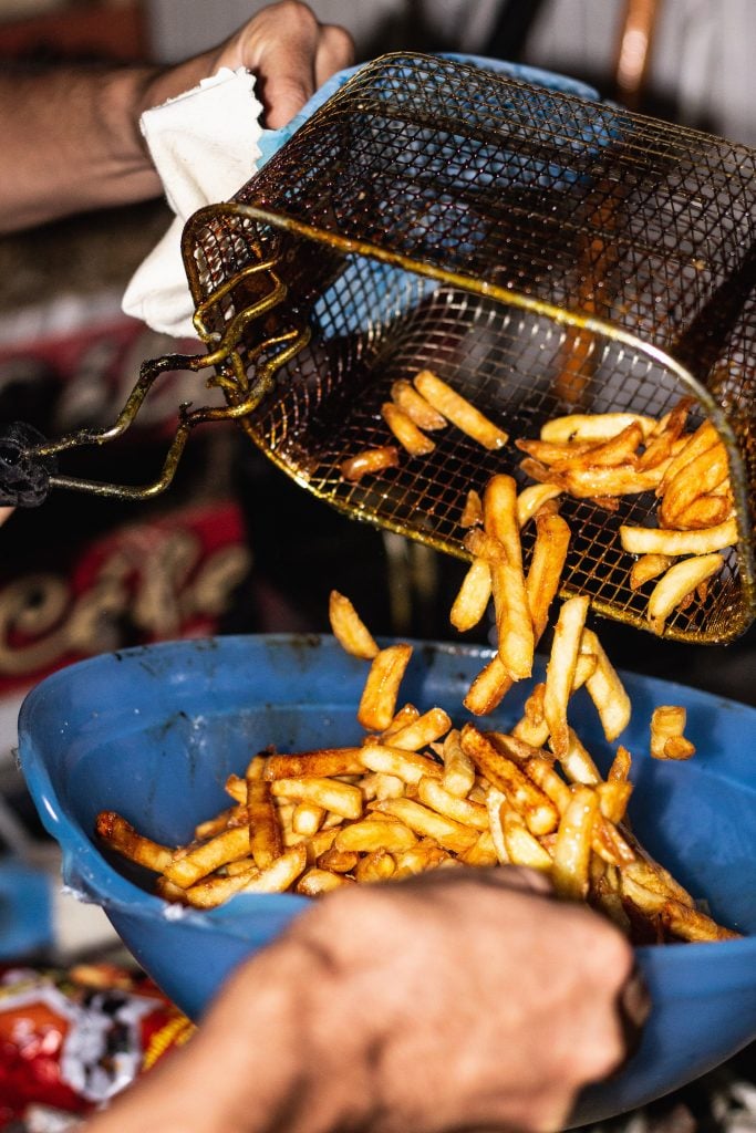 french fries being poured from a fryer basket into a blue bowl.