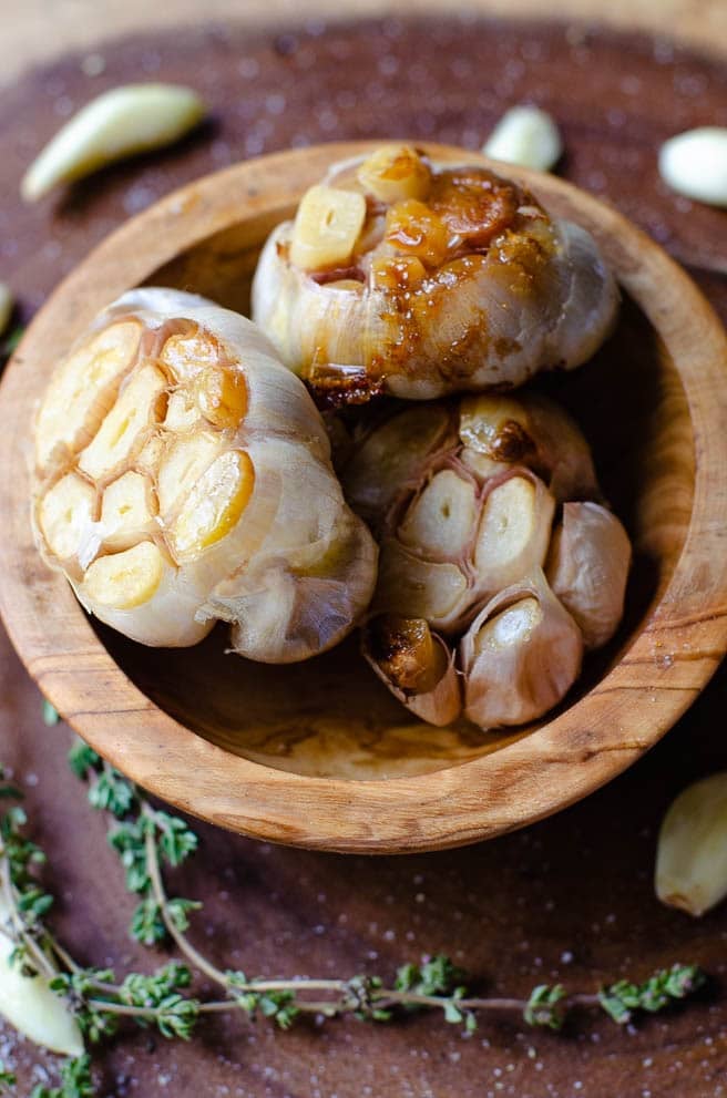 a wooden bowl with three heads of roasted garlic
