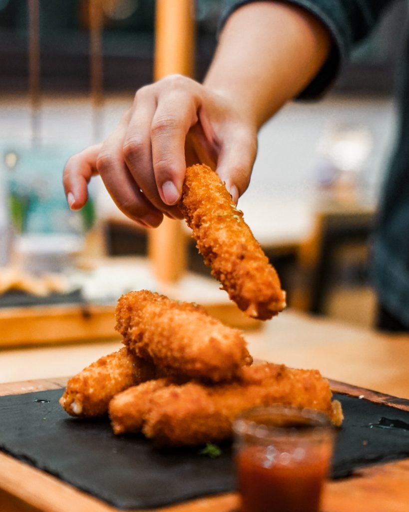 A hand picking up mozzarella sticks from a plate.