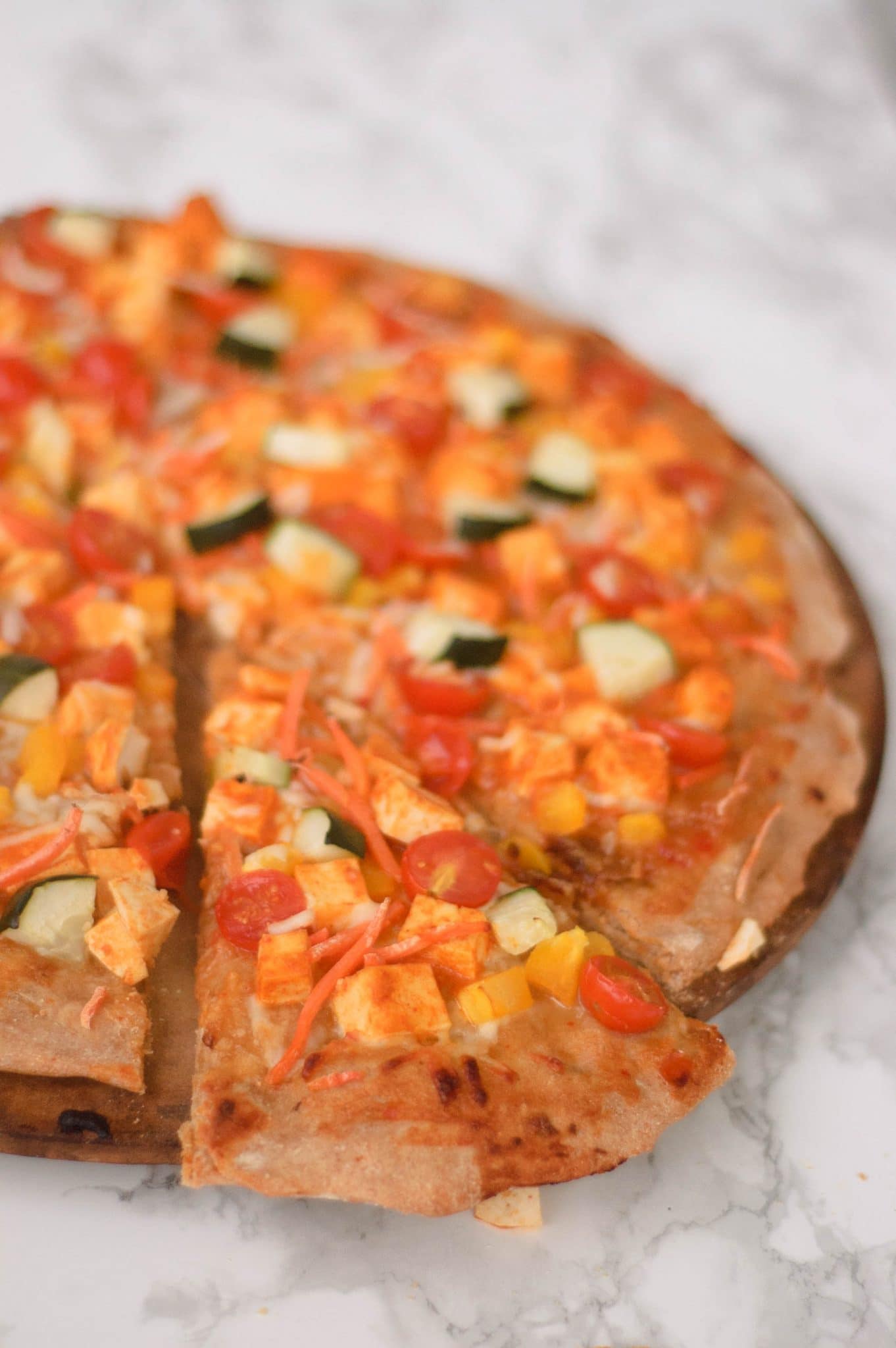 A slice of thai curry pizza pulling away from the whole pie.