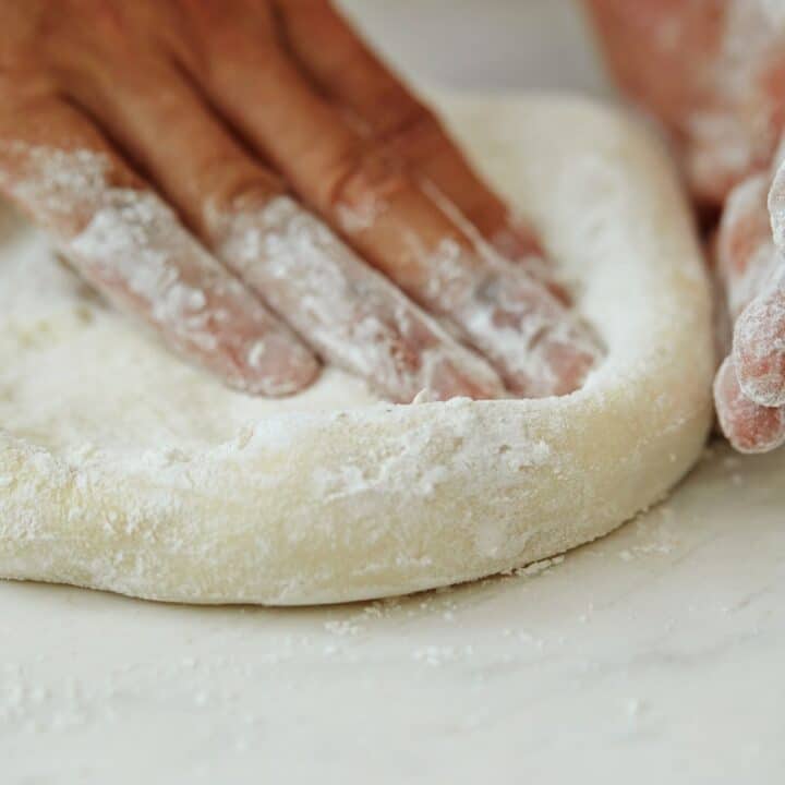 A hand pushing dough to make pizza crust