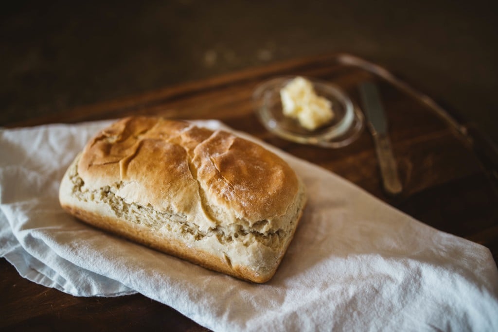 A loaf of white bread on a napkin next to a bowl of butter.