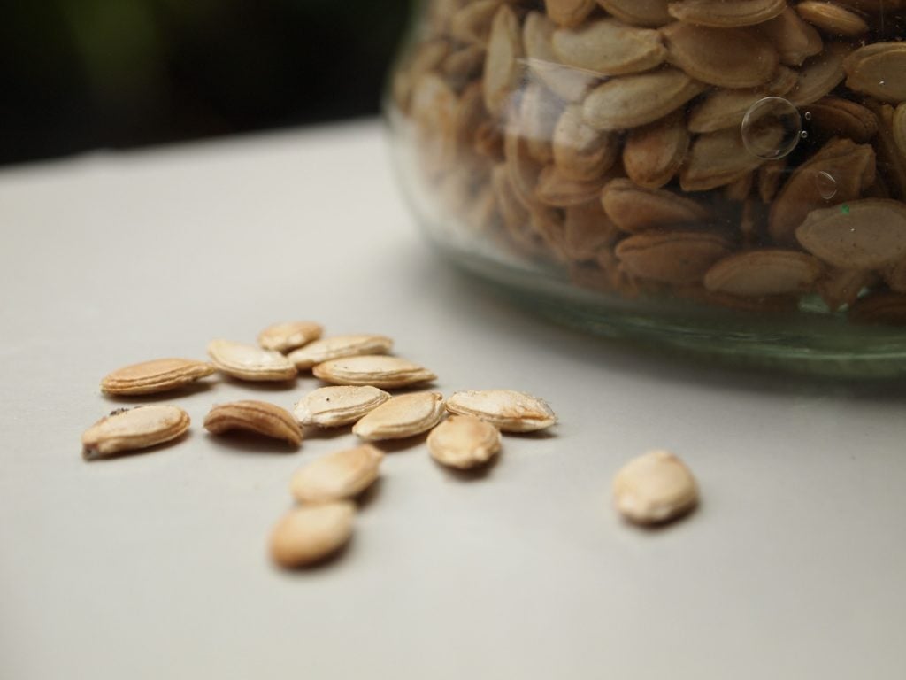a jar of pumpkin seeds with a few loose seeds next to it