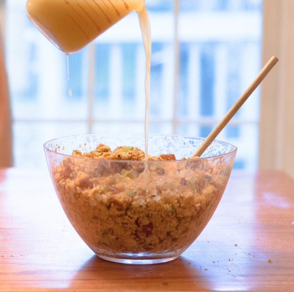 Chicken stock being poured into a large bowl of cornbread stuffing.