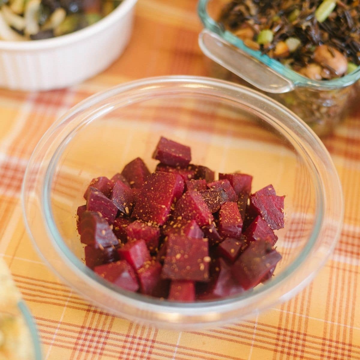 A bowl of roasted cinnamon beets on an autumnal patterned tablecloth