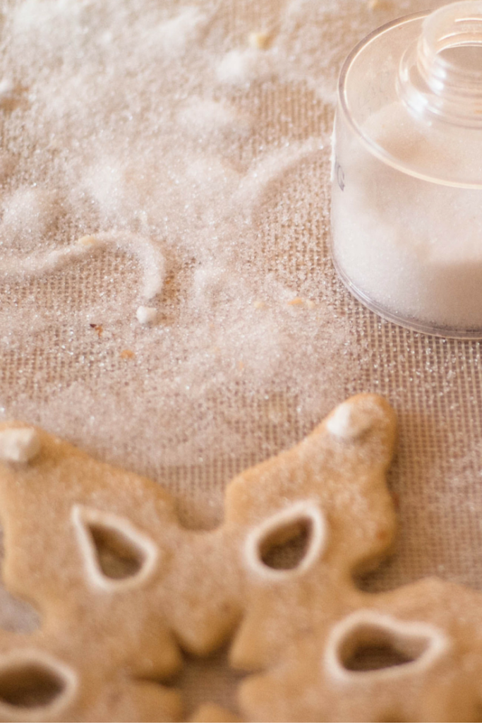 A container of sanding sugar spilled out next to a snowflake cookie.