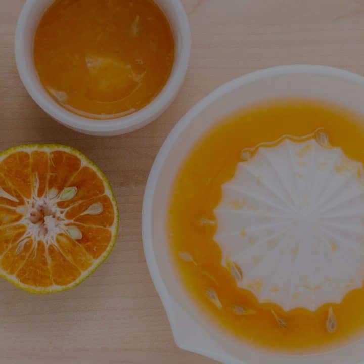A manual citrus juicer filled with orange juice next to a cut orange.