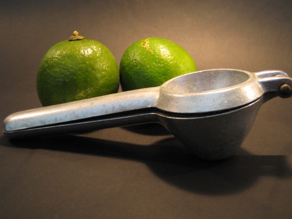 A stainless manual juice press next to two limes.