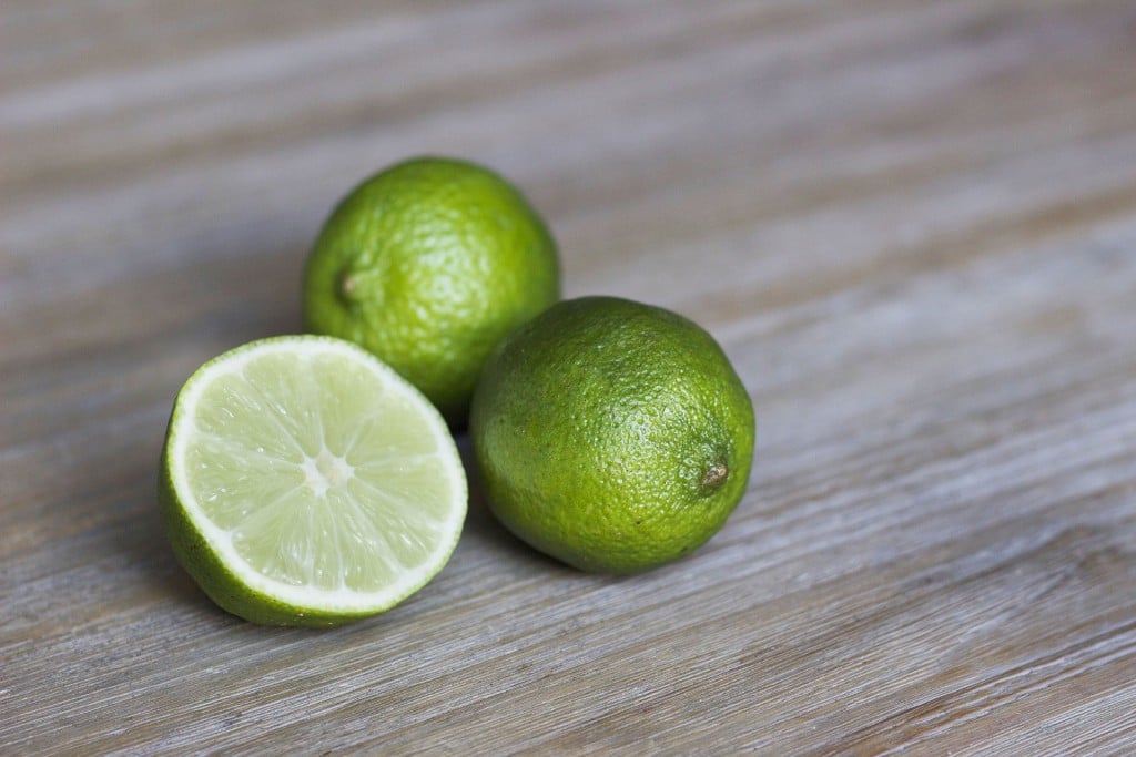 Close up of whole and cut limes on a wooden board.