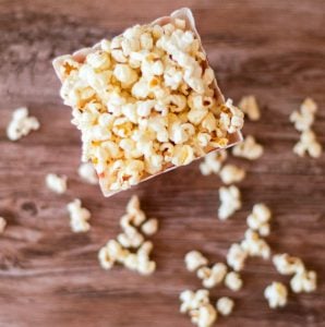 Overhead photo showing homemade buttered popcorn inside a container. Popcorn spills on the table.