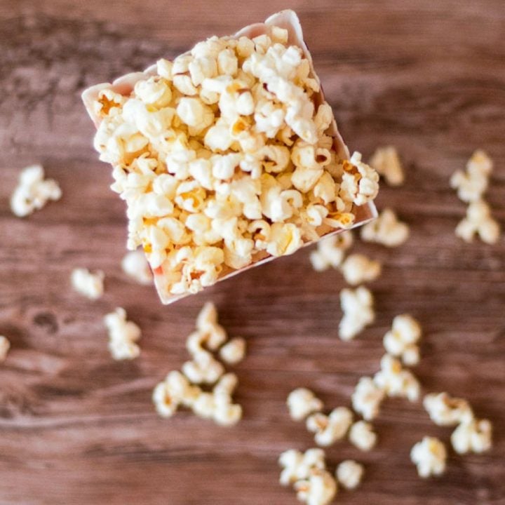Overhead photo showing homemade buttered popcorn inside a container. Popcorn spills on the table.