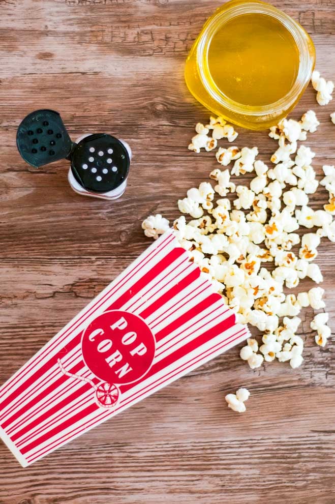 a container of spilled popcorn next to a popcorn salt and a container of clarified butter