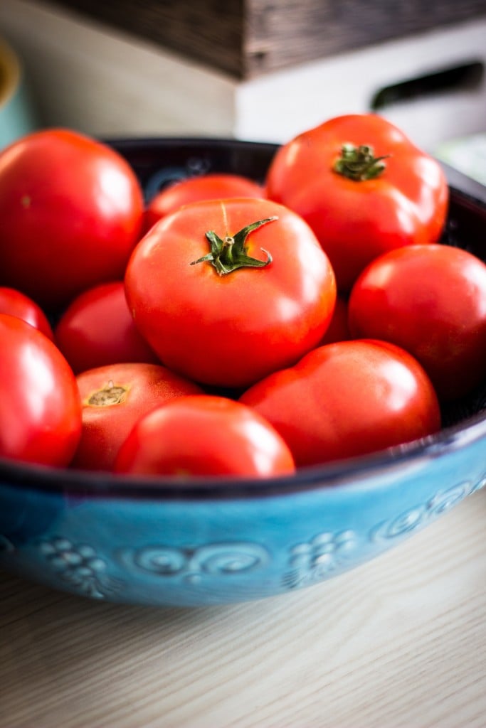 A blue bowl filled with a lot of tomatoes.