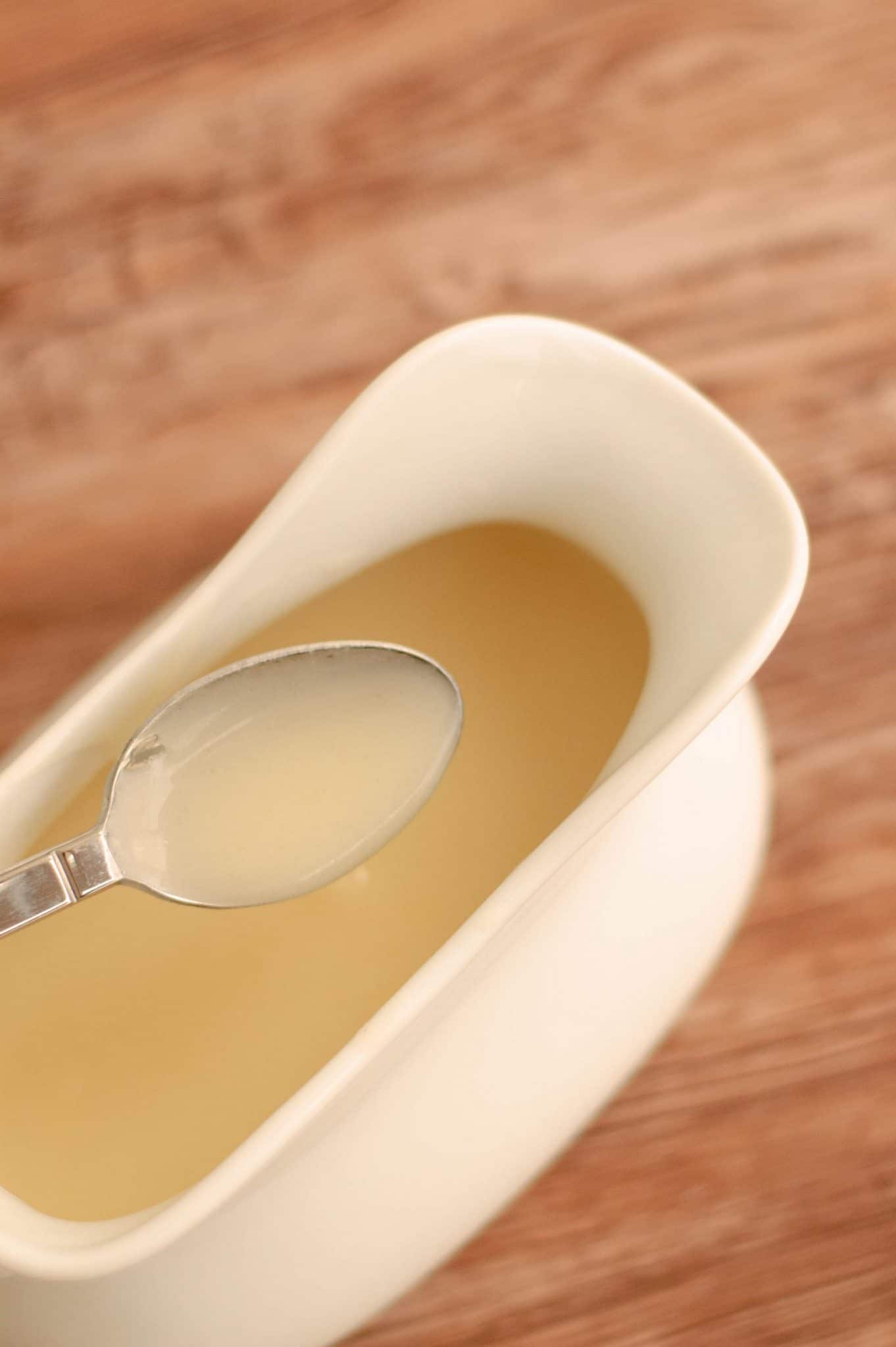 A spoon lifting veloute out of a gravy boat showing the texture and consistency.