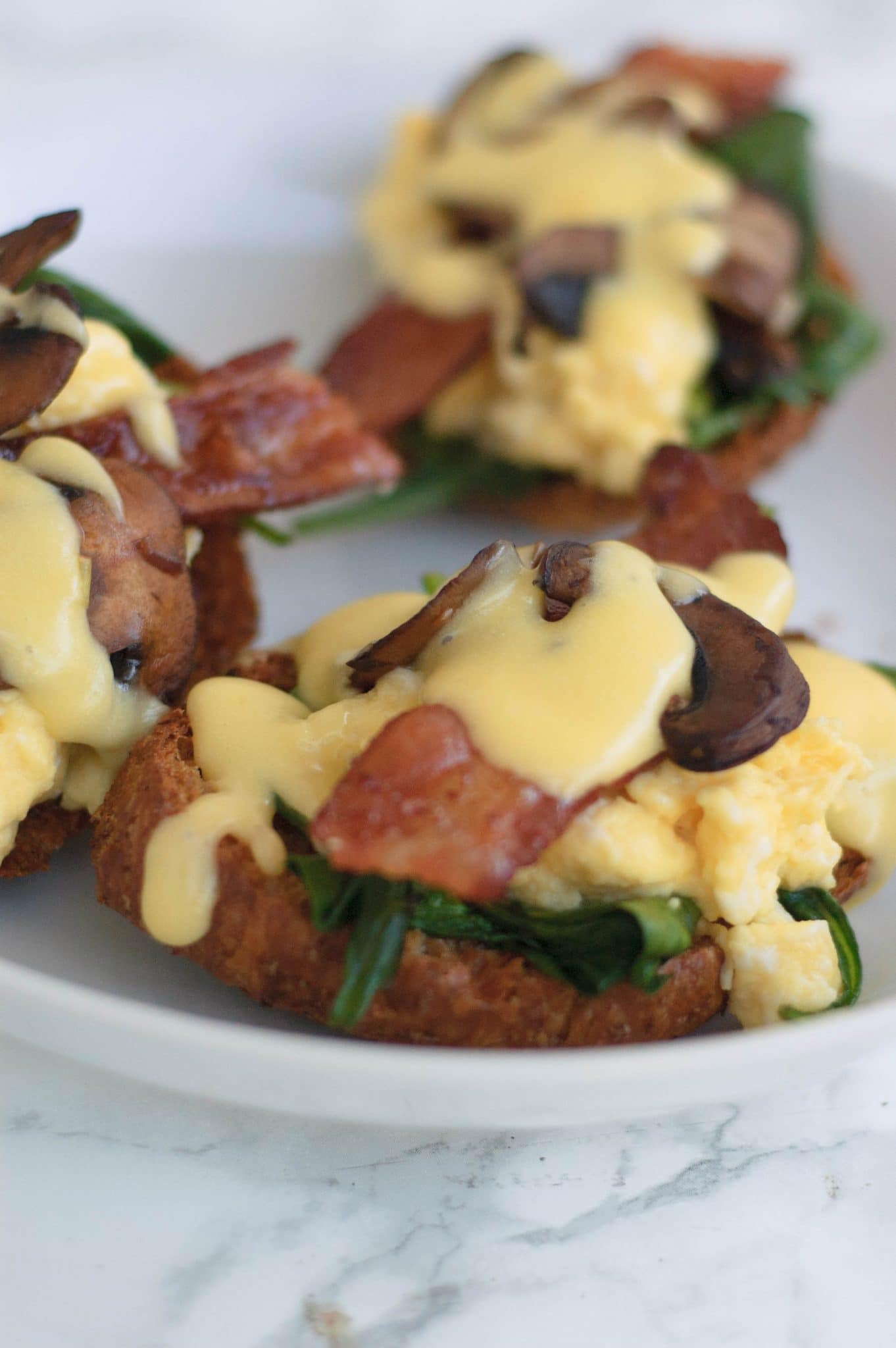 Hollandaise sauce on a crossaint with bacon, mushrooms, and spinach.