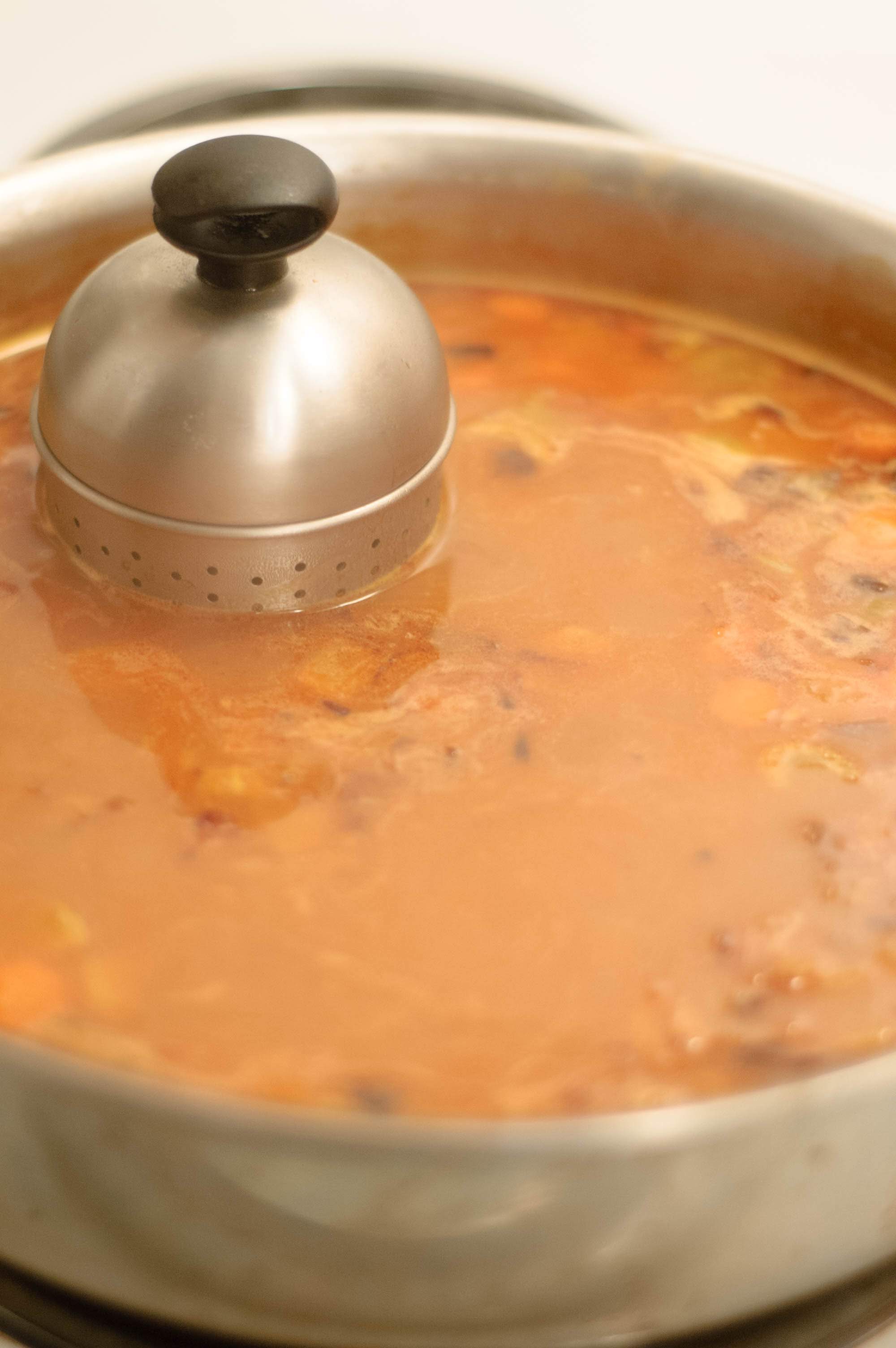 A spice strainer in a simmering sauce pan of espagnole sauce