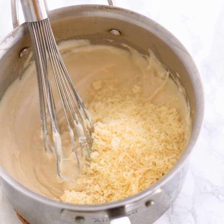 large pot with cheese being mixed into bechamel sauce with a whisk