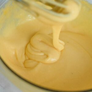 closeup of hollandaise sauce dripping off of a whisk into a bowl.