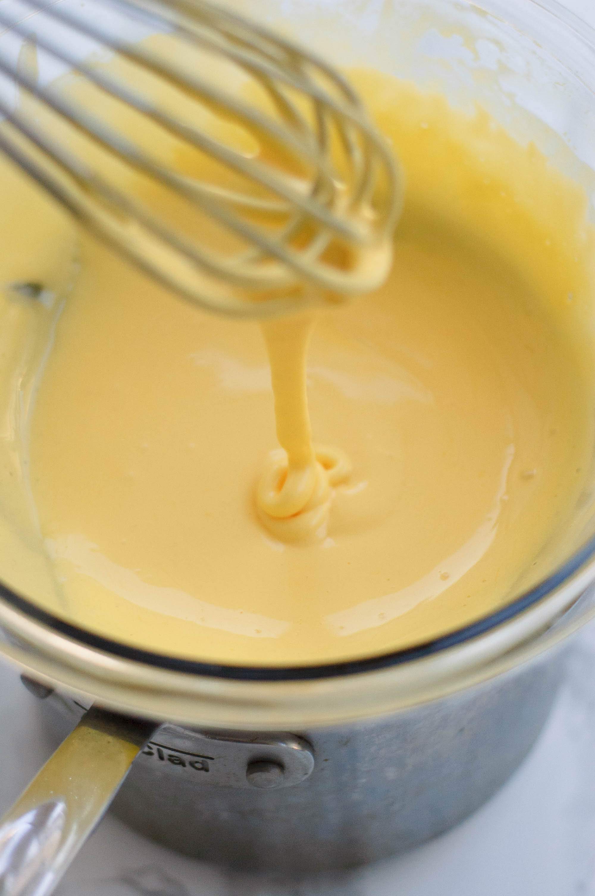 Hollandaise sauce dripping off of a whisk into a bowl of hollandaise sauce.