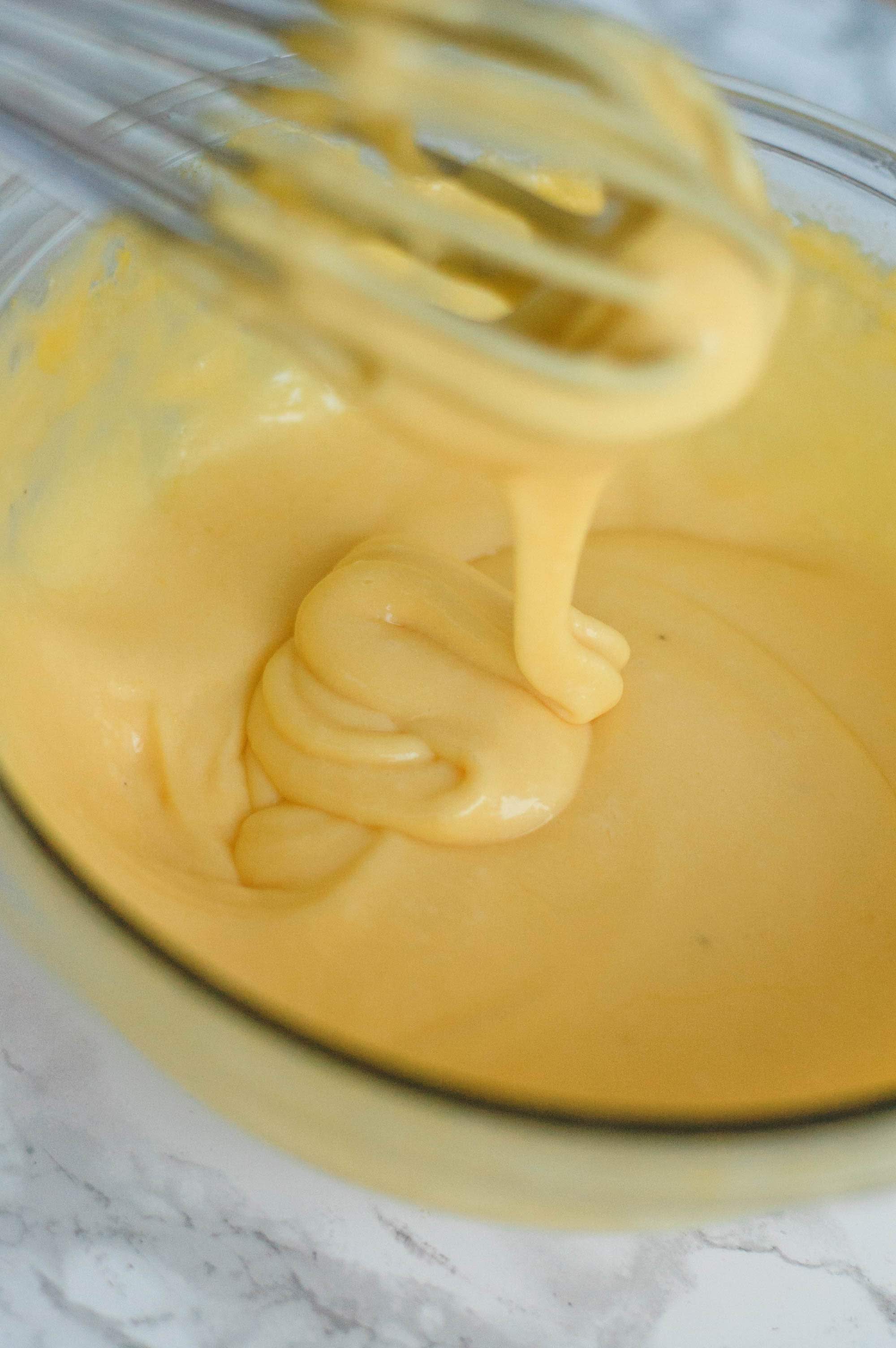 Hollandaise sauce dripping off of a whisk into a bowl.