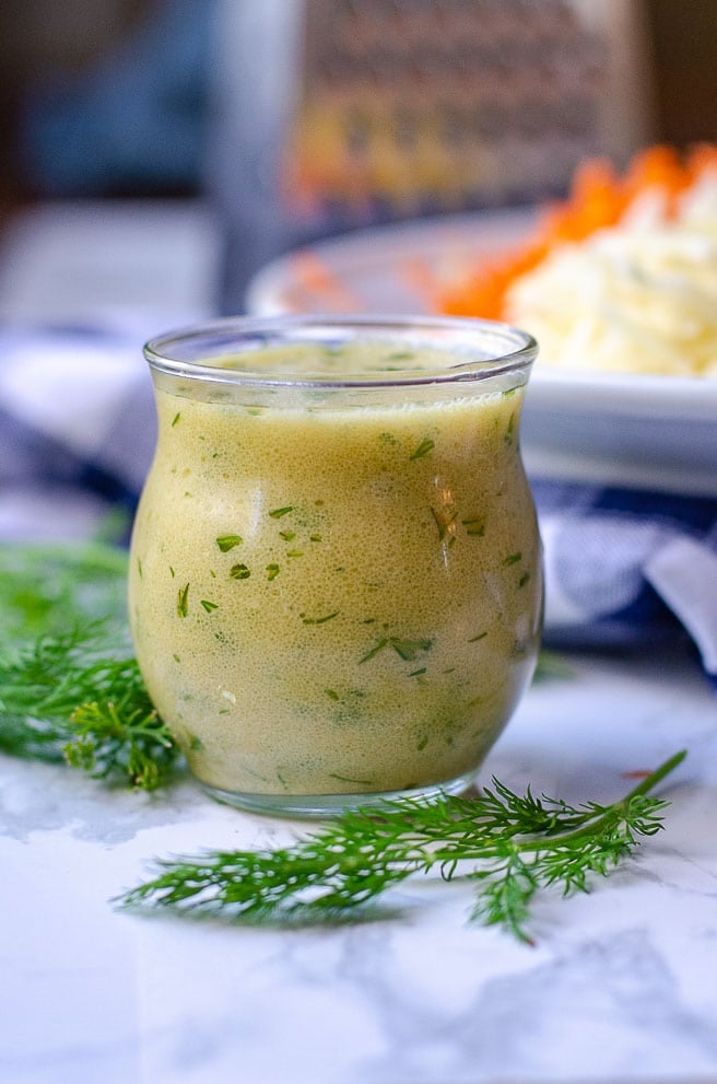 A small jar of salad dressing with fresh herbs in it.