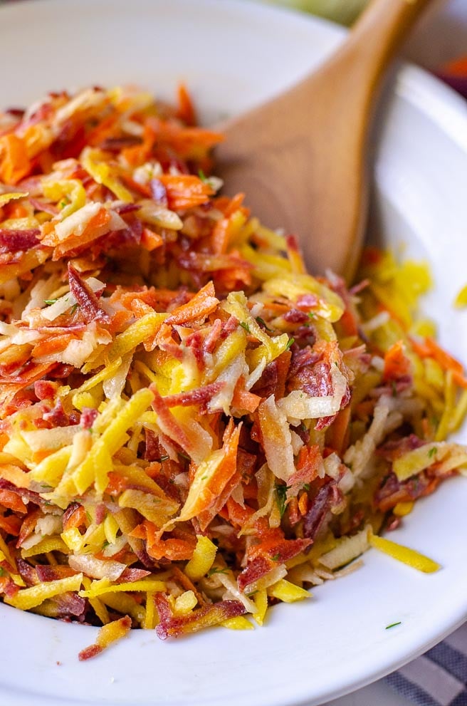 A wooden spoon in a white bowl filled with rainbow carrot salad