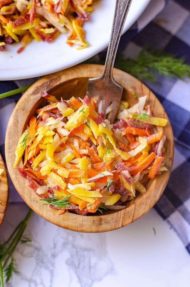 A wooden bowl of rainbow carrot salad with a fork in it.