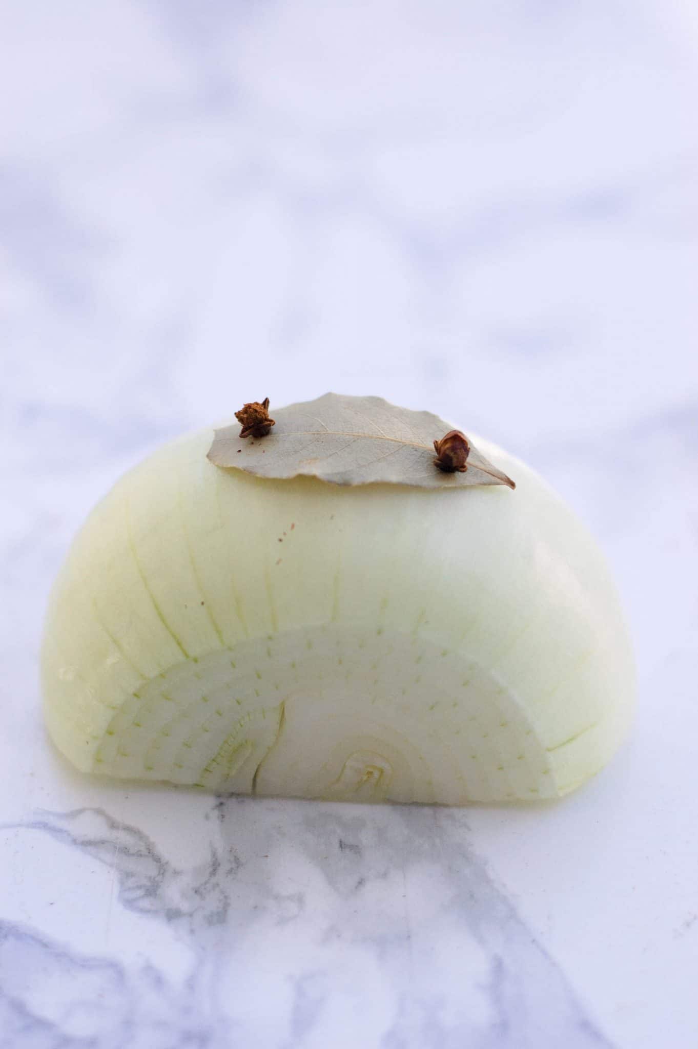 A onion pierced with cloves holding on a bay leaf.