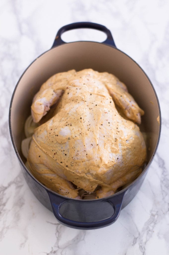 An uncooked whole chicken slathered with mustard and olive oil.