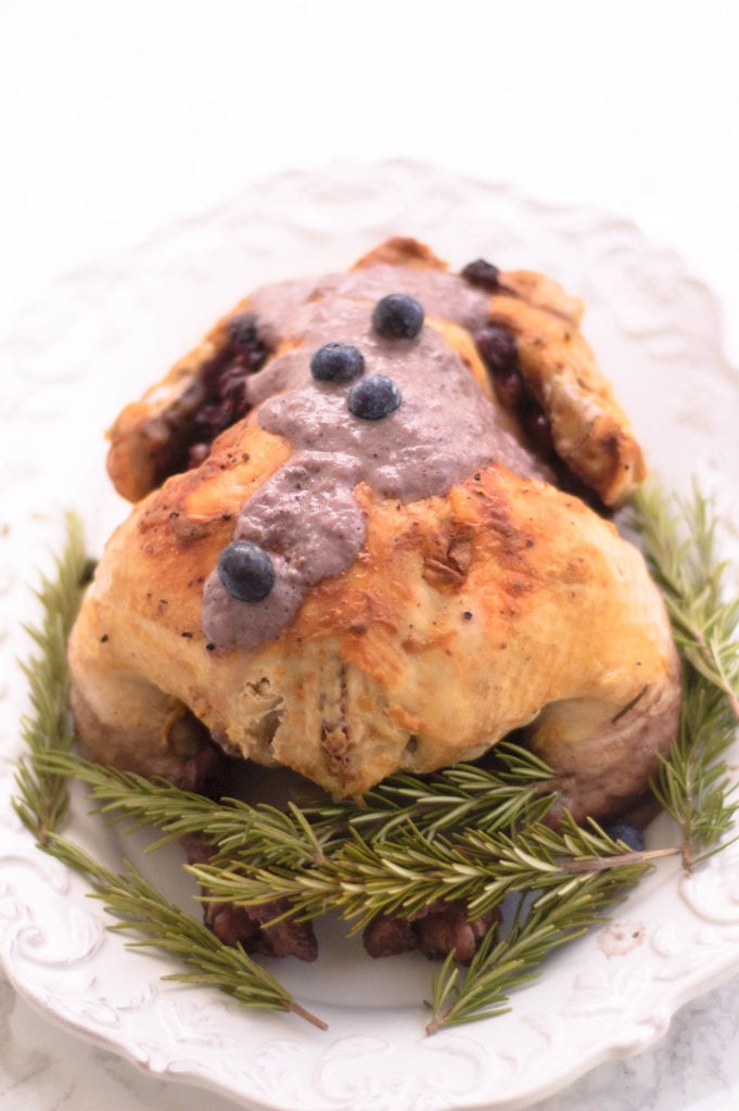 A cooked whole chicken on a serving tray surrounded by fresh rosemary.