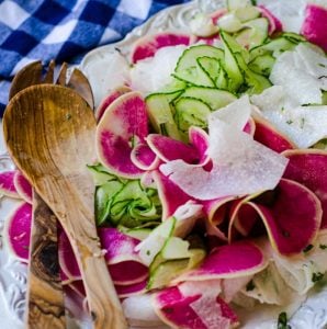 A tossed watermelon radish salad with wooden salad tongs.