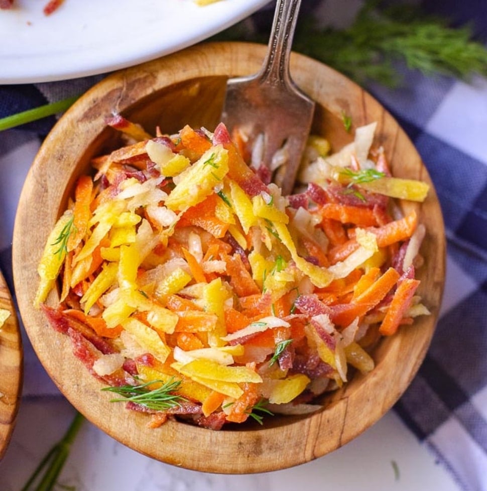 A wooden bowl of rainbow carrot salad with a fork in it.