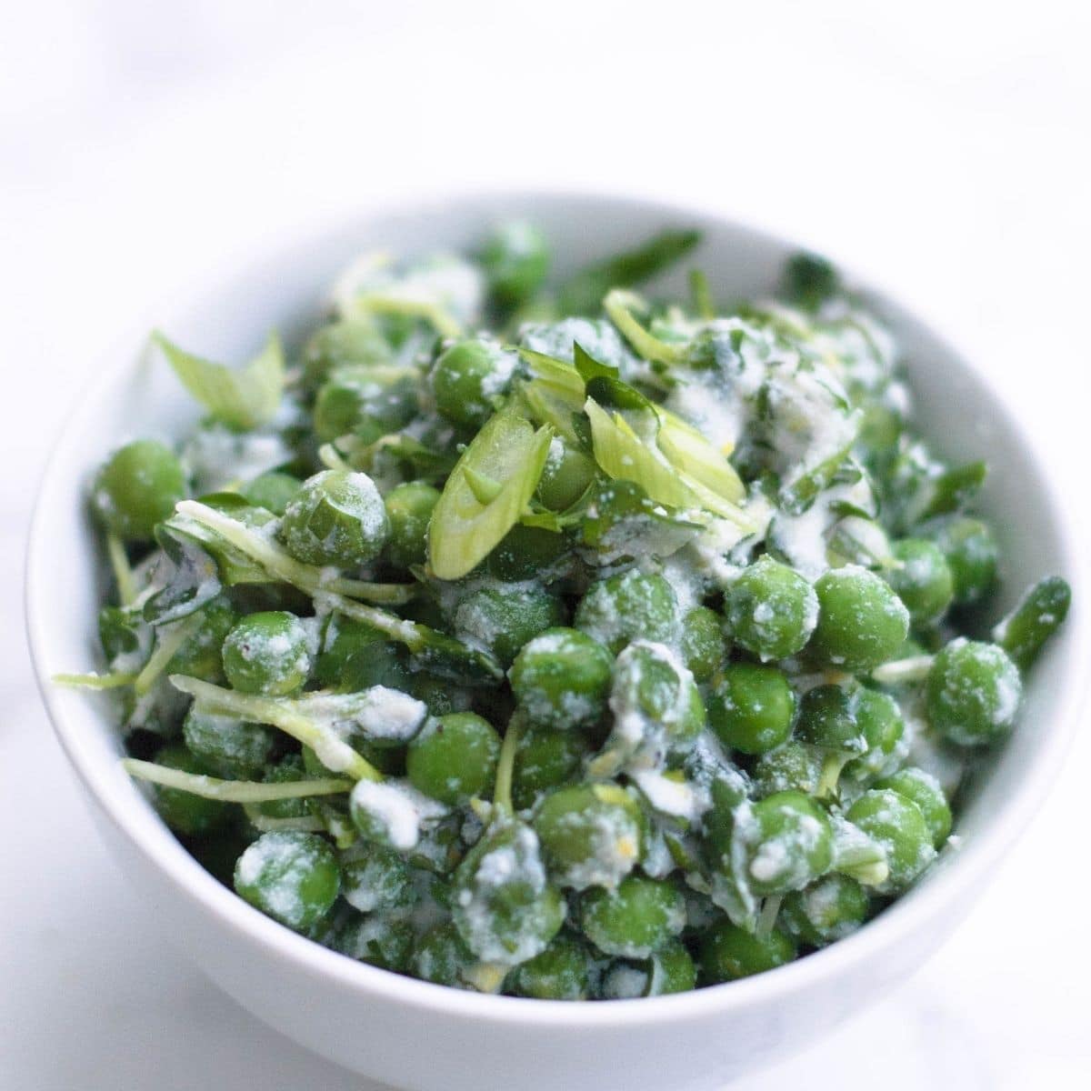A white bowl of spring pea salad with fresh green onions on top.