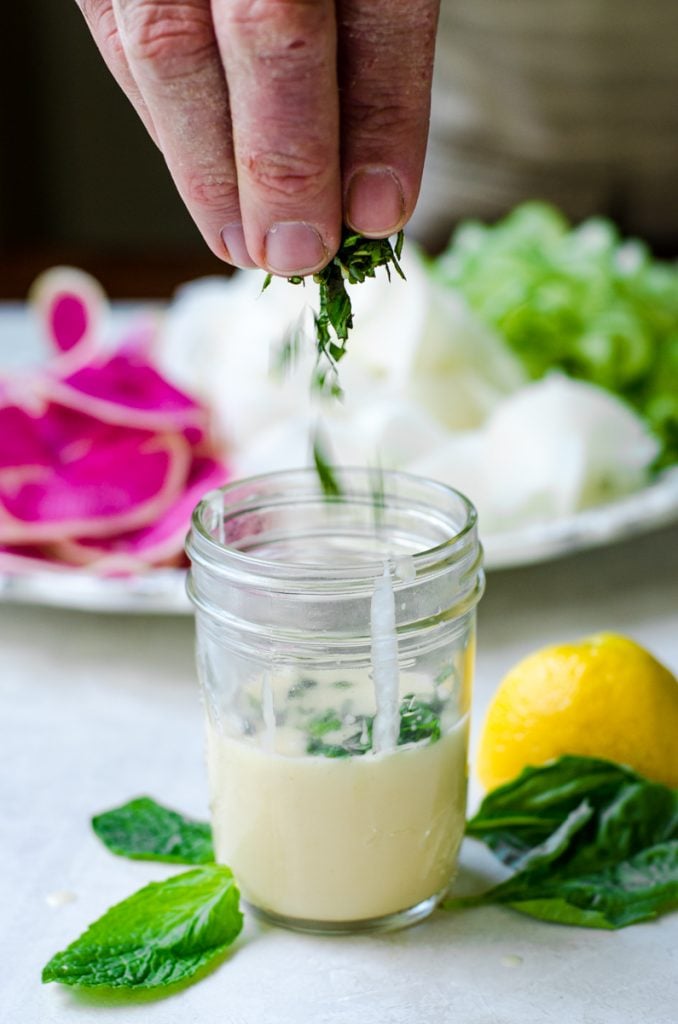 Hands sprinkling fresh herbs into a vinagrette.