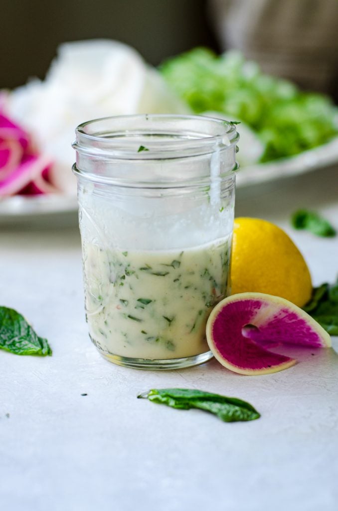 A jar of basil mint vinaigrette surrounded by salad.