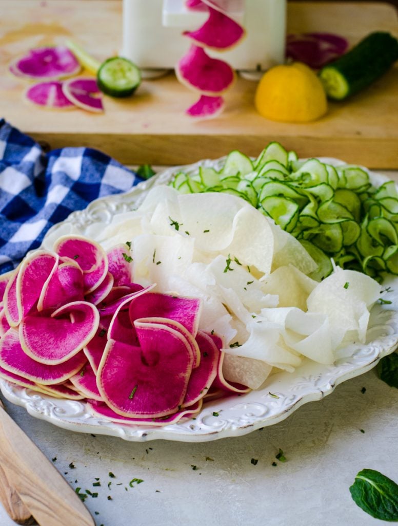 A white plate with ribbons of watermelon radish, jicama, and cucumber next to each other.