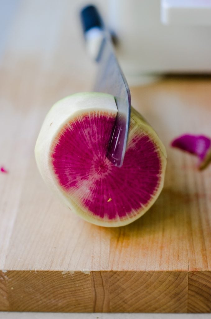 A knife cutting into a watermelon radish.