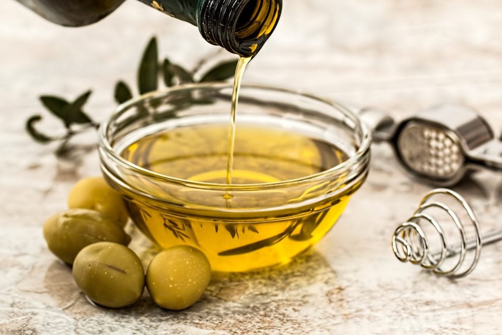 a bottle pouring olive oil into a bowl surrounded by olives.