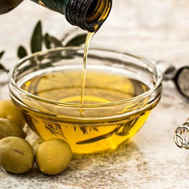 a bottle pouring olive oil into a bowl surrounded by olives.