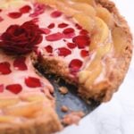rose curd and white peach tart with a piece missing. It has an edible rose in the middle.