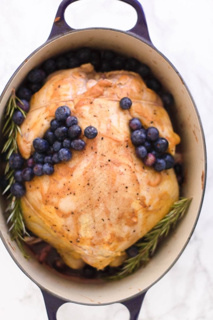 A whole roasted chicken topped with blueberries in a dutch oven.