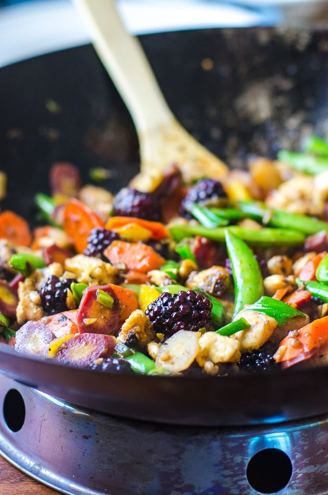 chicken stir fry in a wok with blackberry garnish.