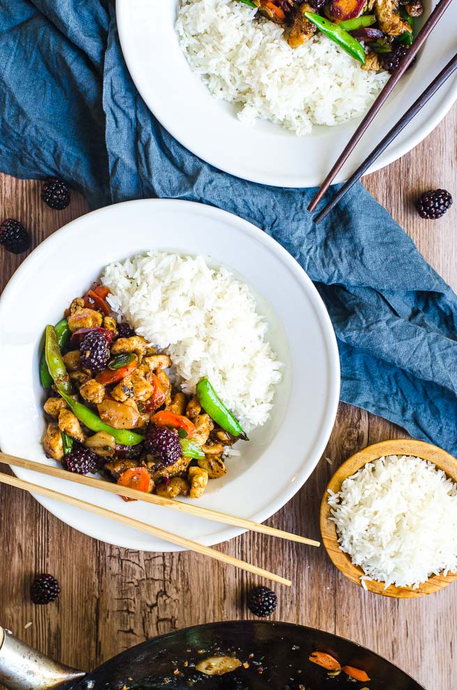 Two bowls of stir fry next to a wok and bowl of white rice.